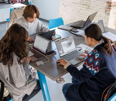 3 students sitting at a table on laptops